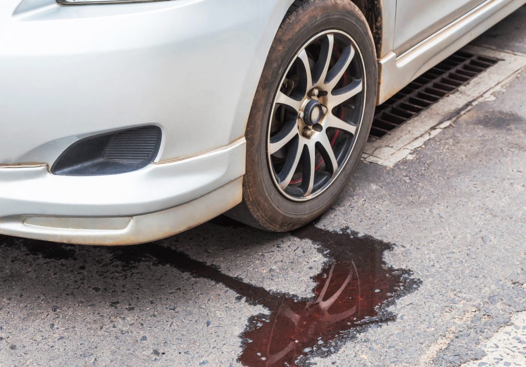 An image of a white parked car with a puddle of transmission fluid underneath it. 