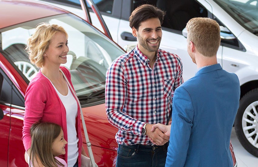 A happy family shaking hands with a dealership salesperson as they close the deal on their new vehicle. 
