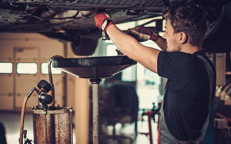 An image of a technician in a repair bay performing a full oil change on a vehicle.
