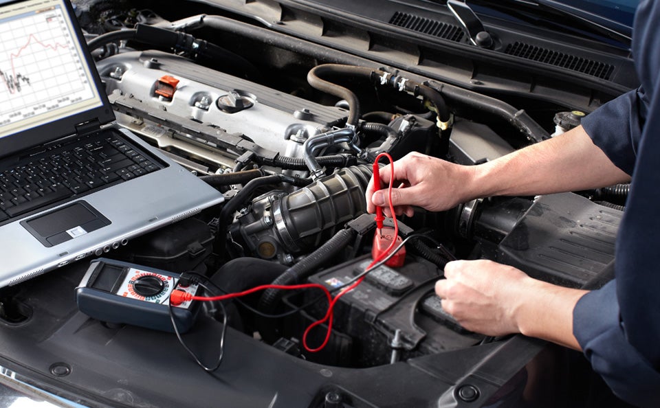 An image of a technician using a multimeter diagnostic tool to test a car battery.