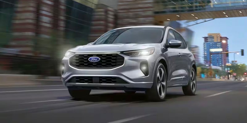 A silver 2024 Ford Escape driving with its headlights on